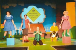 The kids from Snoopy standing in front of their school sign, singing