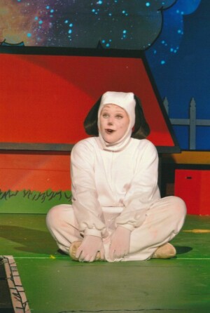 Snoopy sitting cross legged on the stage, singing.