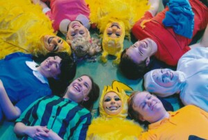 Cast lying on the floor in a circle with photo taken from above them looking down