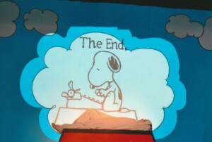 Projection on stage of cartoon Snoopy sitting on his kennel with the words "The End" written above